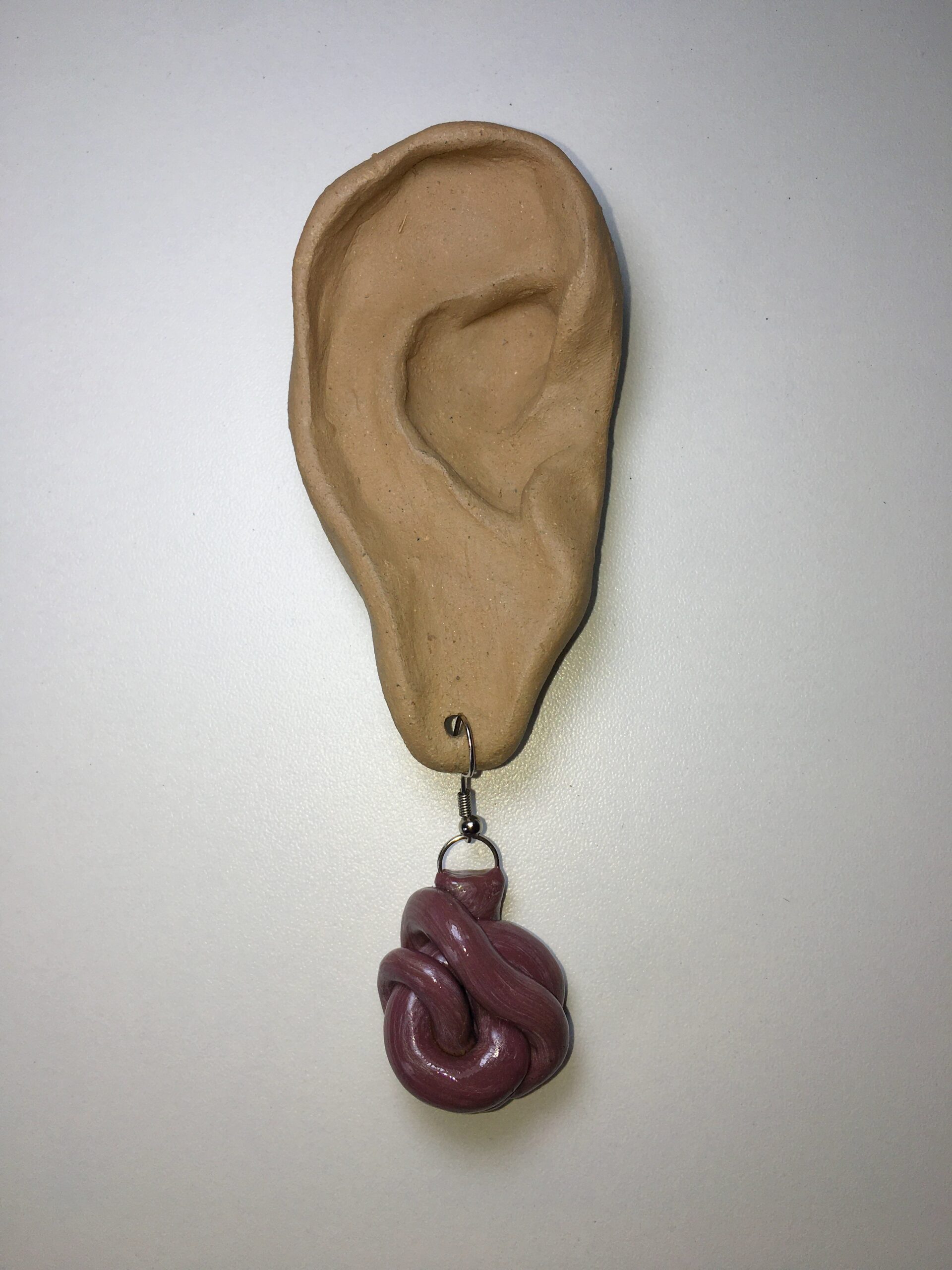 Acessório: Giros Cerebrais 2021; feita de porcelana fria medindo 3,5, pintura em acrílico; brinco ou pingente; a escultura de orelha como objeto expositor também foi feita por CARU, material argila medindo 8cm. [1920X2560 px]